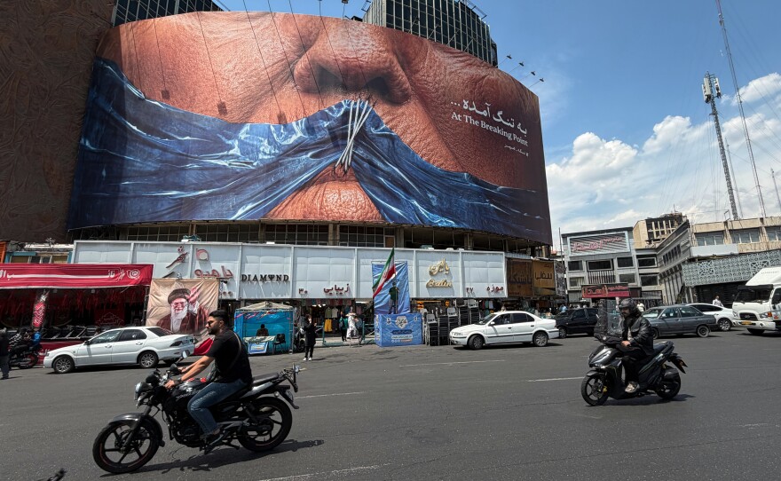 Vehicles drive past a billboard with graphic showing Strait of Hormuz and sewn lips of U.S. President Donald Trump in a square in downtown Tehran, Iran, Saturday, May 2, 2026.