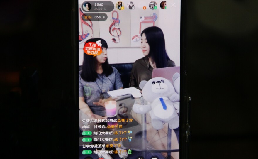 Huang Xian'er (right) is seen on a smartphone, live-streaming a chat with a guest. As they talk, little emoticons — hearts, flowers, gifts — waft across the screen.