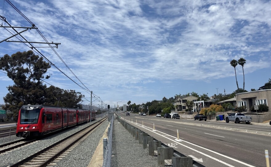 A Blue Line trolley passes by single-family homes in Bay Park, Aug. 25, 2025.