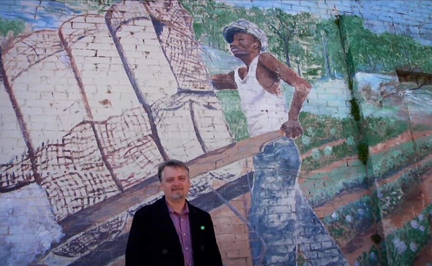 Reporter Chris Tomlinson stands in front of a mural.