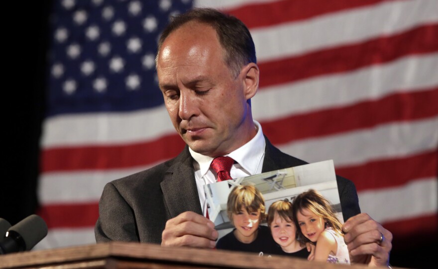 Mark Barden, father of a 7-year-old boy killed at the Sandy Hook Elementary School shooting in Newtown, Conn., holds a photo of his three children during his speech at the state's Democratic Convention, in Melville, N.Y., in 2014. Barden is one of 10 plaintiffs suing Remington Arms Co., the manufacturer of the assault rifle used in the mass murder.