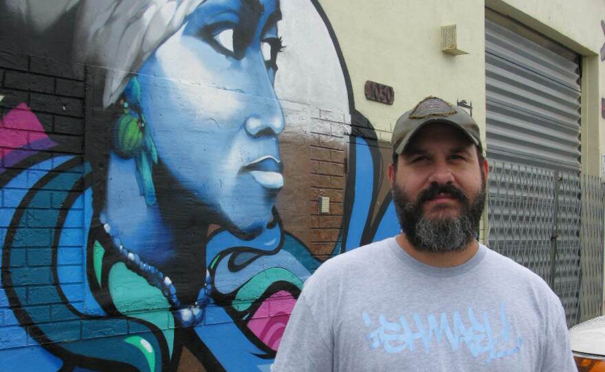 The graffiti artist, Trek6, stands with his symbolic mural.