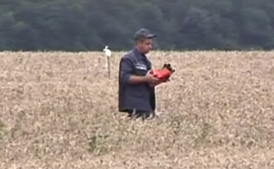 A rescue worker walks across a field carrying what appears to be a flight data recorder at the crash site of Malaysia Airlines Flight MH17 in Hrabove in this still image taken from a video.