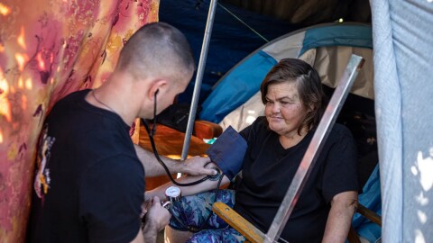 Physician assistant Brett Feldman checks Carla Bolen’s blood pressure at her encampment on the Figueroa Street Viaduct above Highway 110 in Elysian Valley Park in Los Angeles on Nov. 18, 2022.