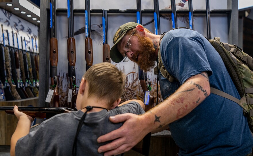 A father helps his son steady a firearm at the National Rifle Association (NRA) annual convention on May 28, 2022, in Houston, Texas. Exposing children to guns comes with risks, but some firearms enthusiasts say they'd prefer to train kids to use guns responsibly.