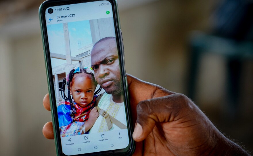 Wuri Bailo Keita, 33, holds a mobile phone showing a picture of himself and his late daughter, Fatoumatta, who is believed to have died of acute kidney failure after ingesting contaminated cough syrup manufactured in India. The family lives in Banjul, Gambia. The photo is from October 10.