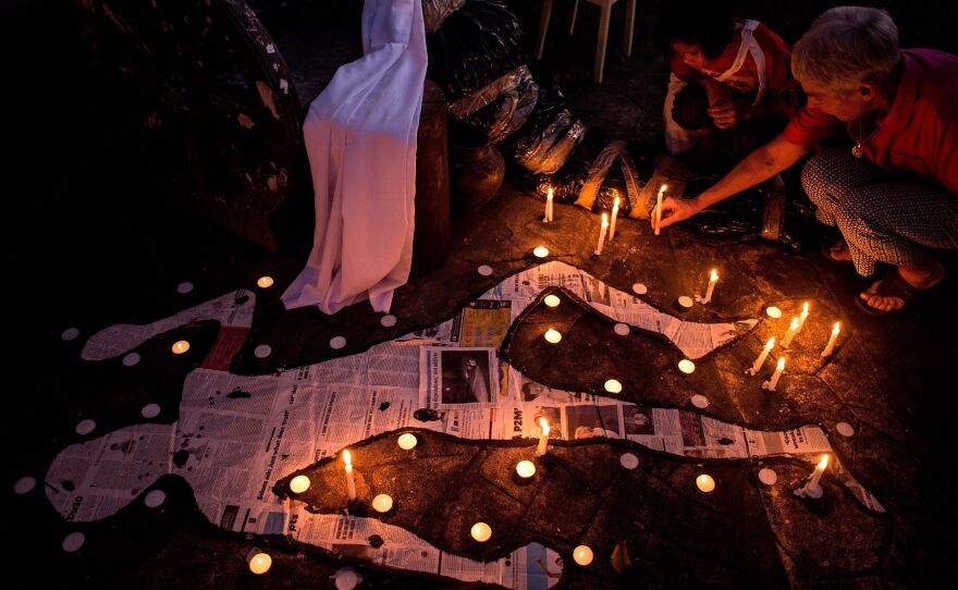 A grandmother and her grandchild light a candle beside mock chalk figure representing an extra judicial killing victim during a prayer rally condemning the government's war on drugs in Manila in 2017.