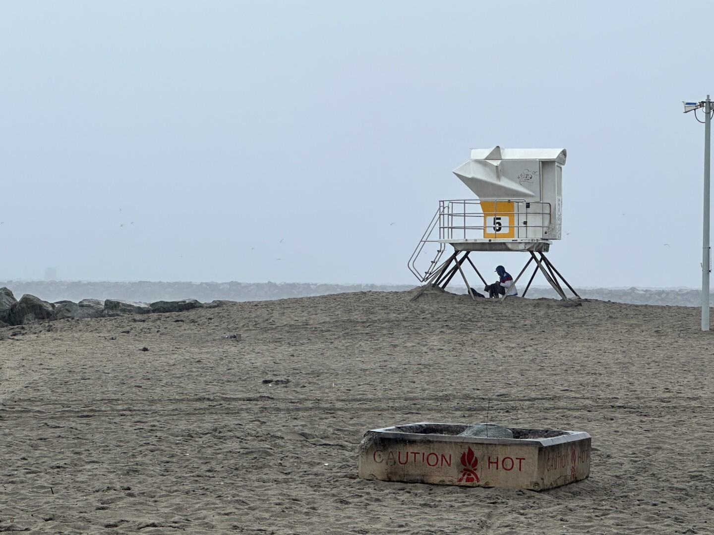 A person finds shelter from the rain under a life guard tower in Ocean Beach, Aug. 20, 2023.