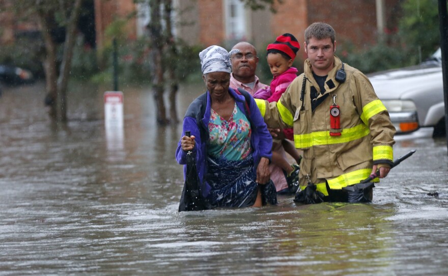 A member of the St. George Fire Department assists residents as they wade through floodwaters from heavy rains in Baton Rouge, La. on Friday.