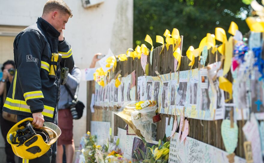A firefighter looks at tributes to presumed victims of the Grenfell Tower fire, after observing a minute's silence at a community center near the apartment building in west London.