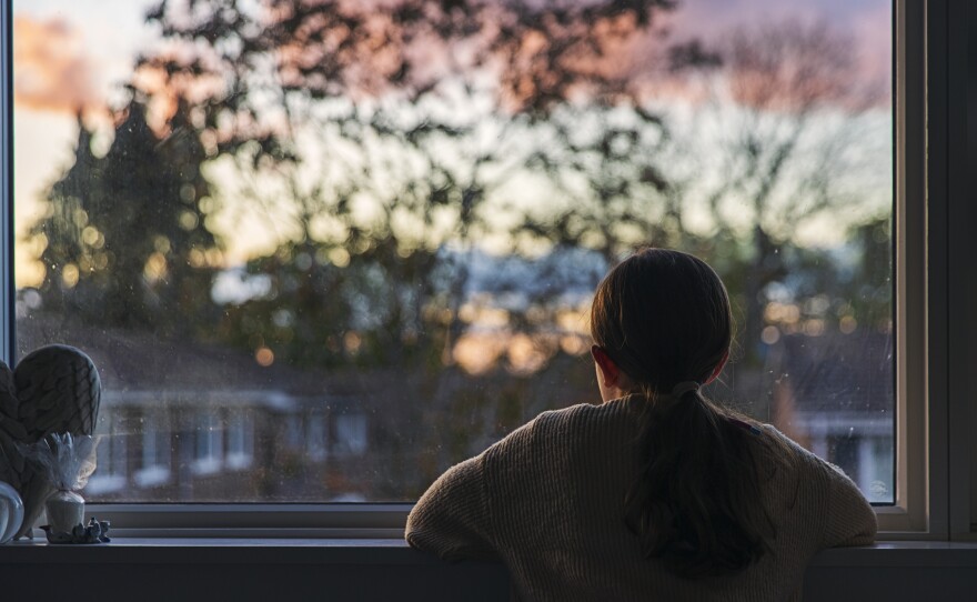 A young girl looks out of her bedroom window as the sun is setting.