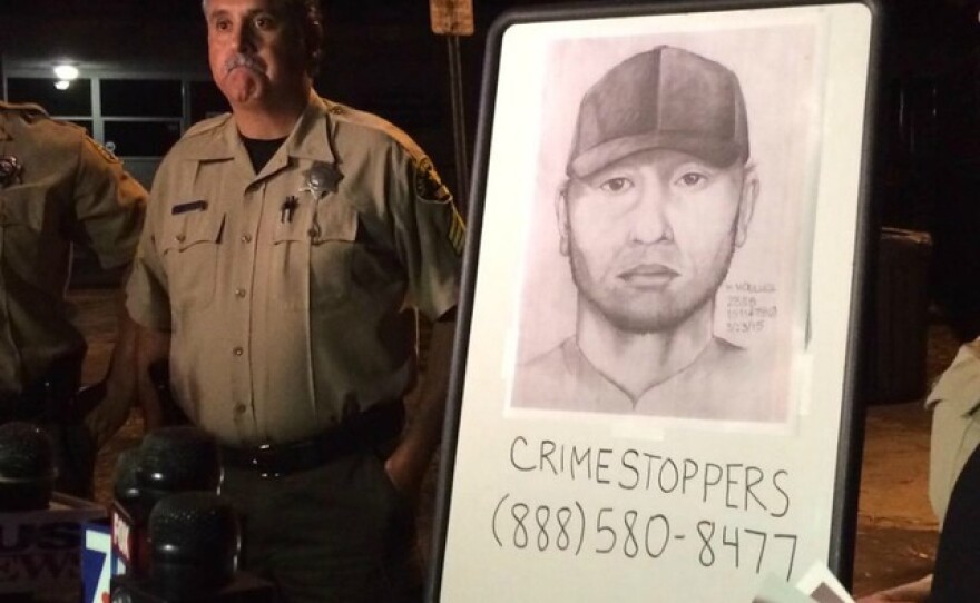 A Sheriff's deputy stands next to a sketch of a man believed to have tried to abduct a girl in Solana Beach, March 25, 2015.