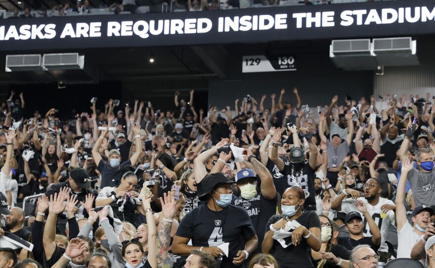 Raiders fans do the wave during a recent preseason game in Las Vegas, as a stadium sign reminds them to wear face masks. The team now says spectators will have to show proof of vaccination — and that no masks will be required for those who have been vaccinated.