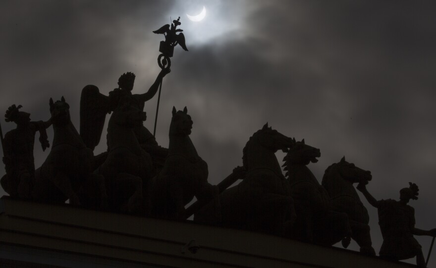 The moon blocks part of the sun during the eclipse as seen over a statue at the one of the city landmarks, the General Staff Headquarters in St. Petersburg, Russia.