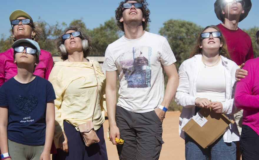 People wear protective glasses as they look up at a solar eclipse in Exmouth, Australia, Thursday, April 20, 2023.