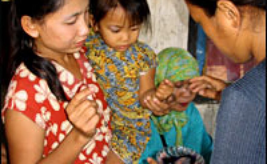 A health worker prepares to dip a young girl's finger in ink. Health workers use the ink marks to help keep track of the number of children vaccinated children in a given village.