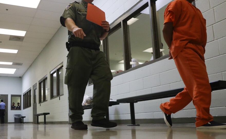 A guard walks with a detainee in the intake area at the Adelanto ICE Processing Center in 2019. A previously confidential report obtained by NPR found "negligent" medical care and other problems at the facility.