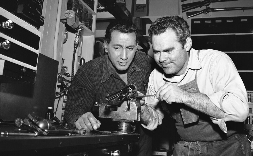 In this photo from a Hollywood studio gun department in 1958, Rodd Redwing (left) checks the final adjustment that Bob Lane is making on a six-gun. Redwing is an actor and a teacher of western gun handling. Lane is one of the men who repair and service the many guns in the studio arsenal.