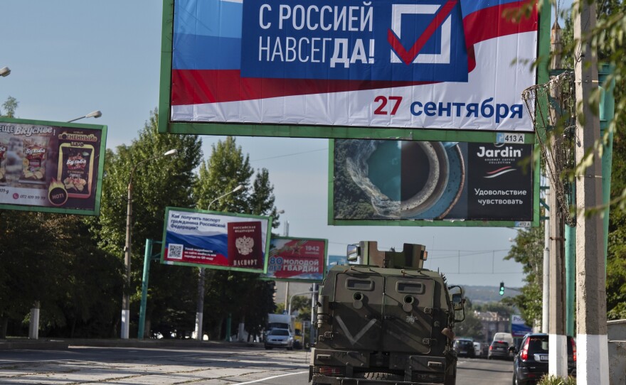 A military vehicle drives along a street with a billboard that reads: "With Russia forever, September 27", in Luhansk, controlled by Russia-backed separatists, eastern Ukraine, Sept. 22, 2022.