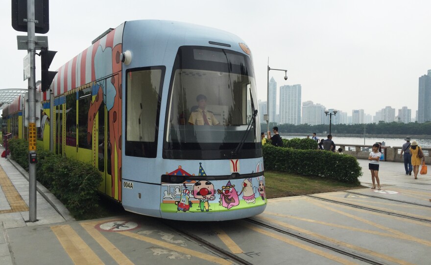 A circus-themed streetcar approaches a pedestrian crosswalk in Guangzhou, China.