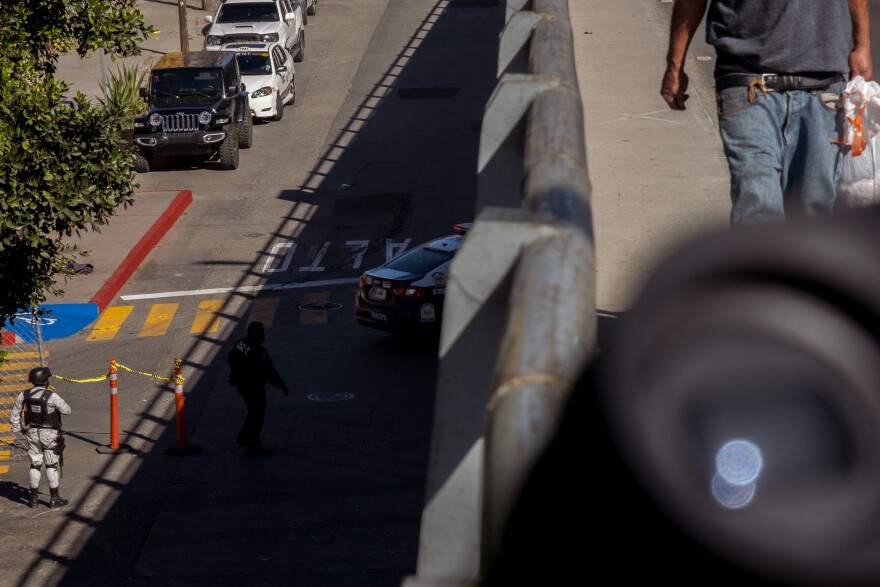 Members of Mexico's National Guard secure the front entrance to the now empty migrant camp while a pedestrian walks the highway bridge over them, Tijuana, February 7, 2022.