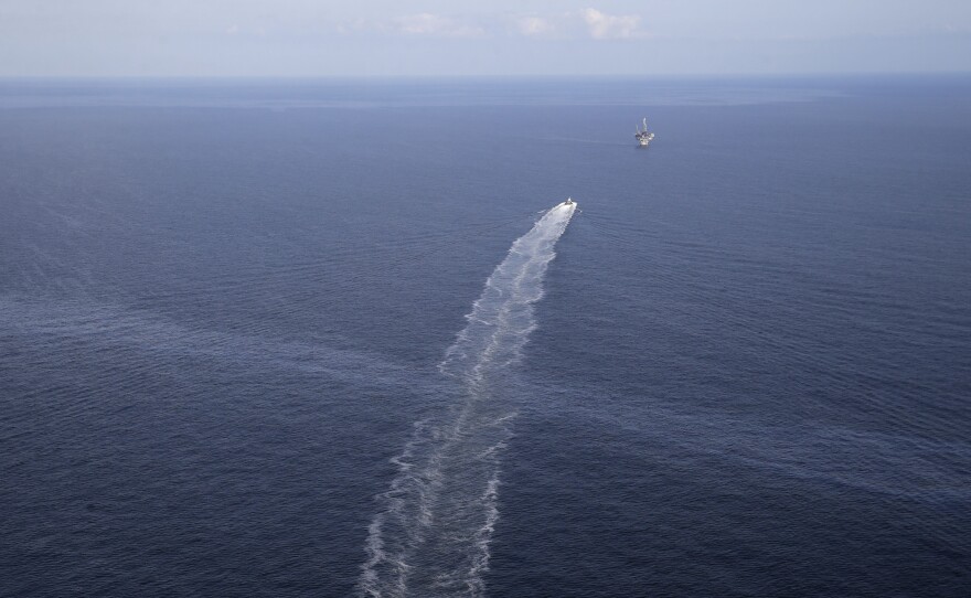 The wake of a supply vessel heading toward a working platform crosses over an oil sheen drifting from the site of the former Taylor Energy oil rig in the Gulf of Mexico in 2015. The Coast Guard says it has contained the oil spill.