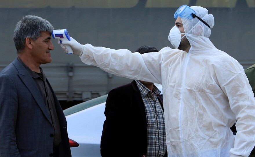 As the coronavirus that causes COVID-19 spreads to more areas, a health worker checks a man's temperature at a checkpoint on the outskirts of Duhok, Iraq, last Tuesday.