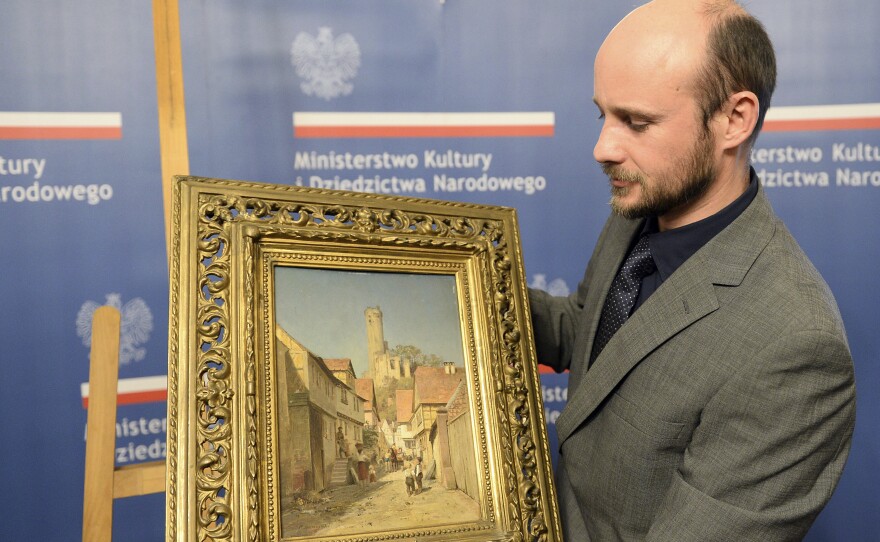 A museum worker carries a 19th century painting by Polish artist Robert Sliwinski during a ceremony Wednesday in Warsaw, Poland. The work was looted by the Nazis during World War II and recently recovered in the U.S. by the FBI.