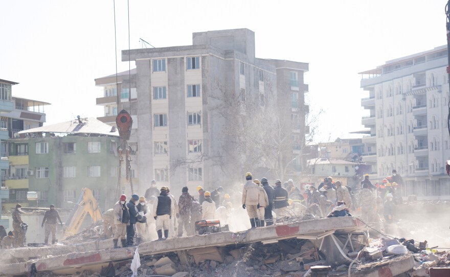 Workers stand in the debris and dust of an apartment building where members of the Demir family lived, as they dig through it looking for people who were in the building when it collapsed.