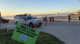A sign in the sand reminds beachgoers to wear a mask at Moonlight State Beach in Encinitas, Dec. 15, 2020.