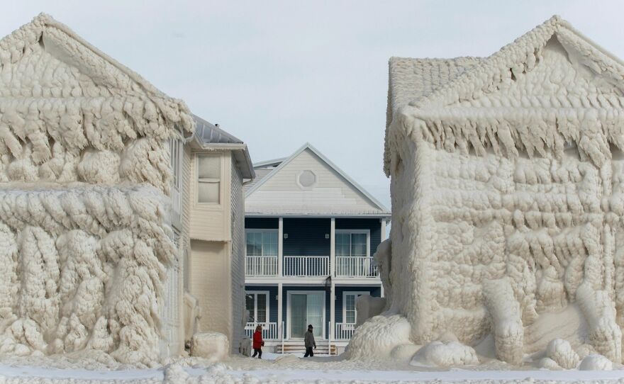 People walk between frozen homes in the waterfront community of Crystal Beach in Fort Erie, Ontario, Canada.
