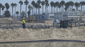 Heavy machinery is used to build sand barriers to contain oil washed up in Huntington Beach, Calif., Sunday, Oct. 3, 2021. 