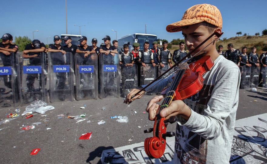 A refugee boy plays a violin as hundreds of migrants are blocked from marching down a highway towards Turkey's western border with Greece and Bulgaria, on Saturday. Turkey has some 2 million refugees, mostly from Syria, but says they will not be allowed to settle permanently in the country.