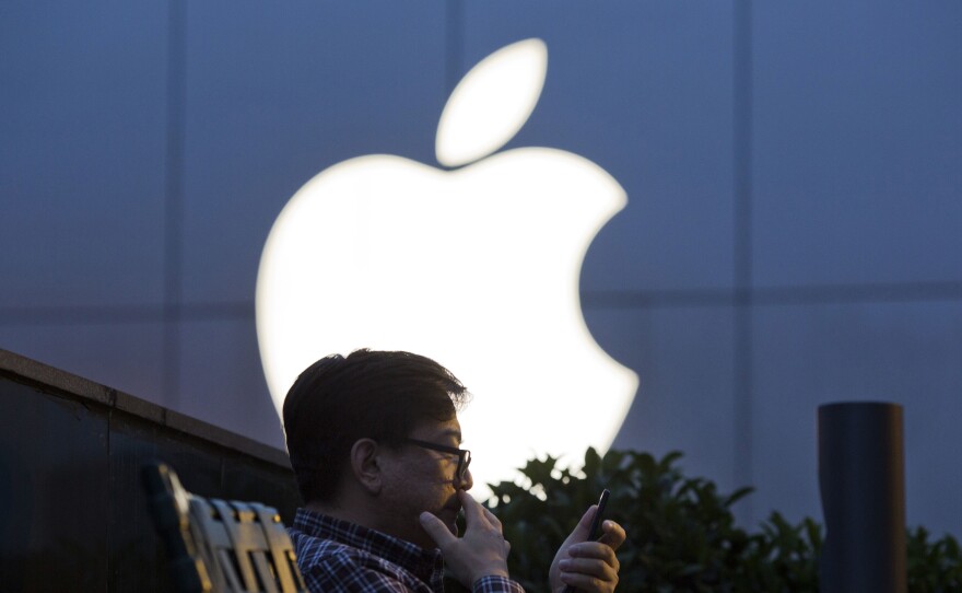 A man uses his mobile phone near an Apple store logo in Beijing.