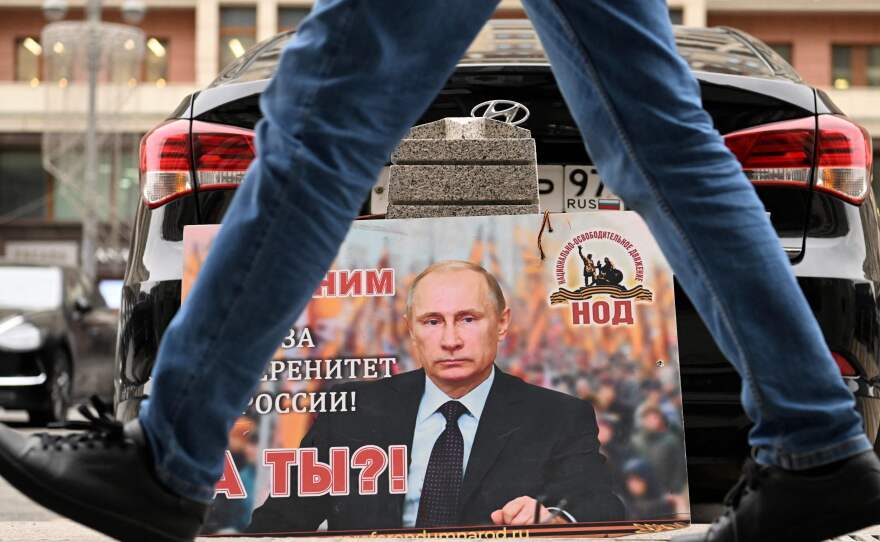 A placard featuring an image of Russian President Vladimir Putin and reading "We are with him for the sovereignty of Russia! And you?" is seen left in front of the Russian State Duma building in central Moscow on February 24, 2022.