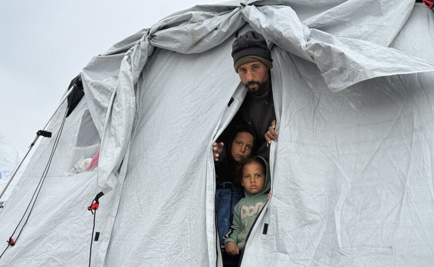 Raed el-Ghazawi and his children stand in a tent in Gaza City on Dec. 11, 2025. The family of five says the tent is freezing cold and damp from winter rainstorms.