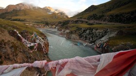 Tibetan prayer flags hang from a bridge crossing the Mekong River at sunrise. The river is known in Tibetan as the Dzachu, or "river of rocks," and in Chinese as the Lancang Jiang, or "turbulent river."