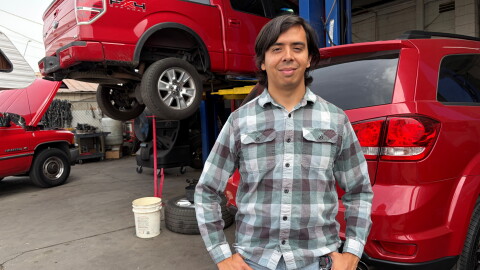 Guadalupe Higuera stands in front of trucks being repaired at his family's shop in Phoenix.