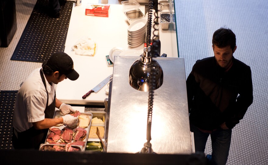 Nick Wiseman, partner at DGS Delicatessen, inspects the kitchen as an employee prepares pastrami sandwiches for lunch.