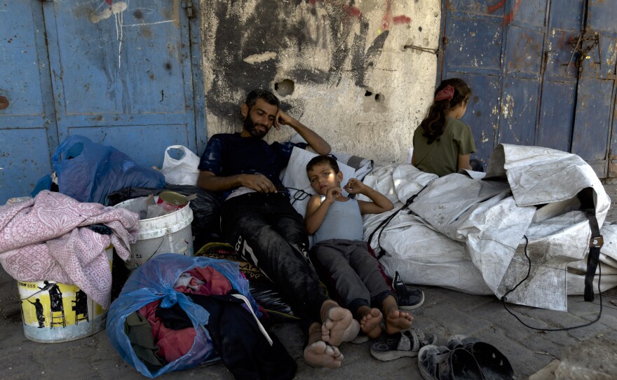 A Palestinian man rests with his children and few belongings on the sidewalk in the Sheikh Radwan neighborhood of Gaza City after fleeing on foot an Israeli assault on his neighborhood further north, on Aug. 26.