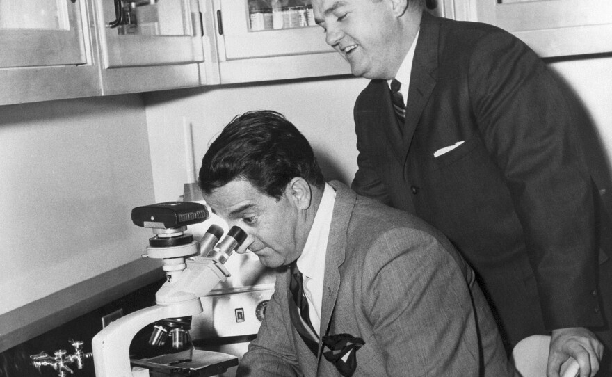 Danny Thomas looks through a microscope as Dr. Donald Pinkel stands just behind him.