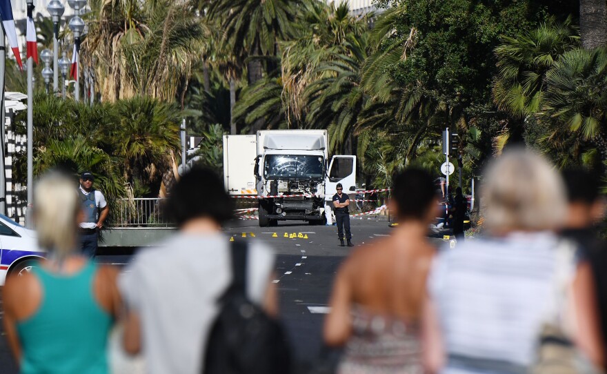 People look at a truck guarded by the police on the Promenade des Anglais seafront in Nice, France, on Friday, hours after it drove into a crowd watching a fireworks display. More than 80 people were killed as a truck drove through crowds gathered to watch a firework display during Bastille Day celebrations.