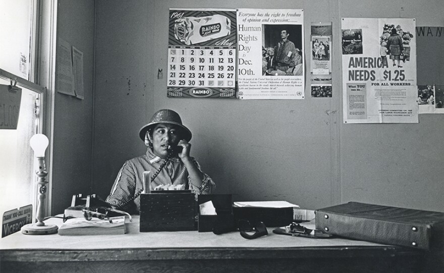 Migrant mother Maria Moreno became the first farmworker woman in America to be hired as a union organizer. Wearing “jungle” (safari) hat, Maria makes a phone call in the office of the Agricultural Workers Organizing Committee, Fresno, Calif. 1961.