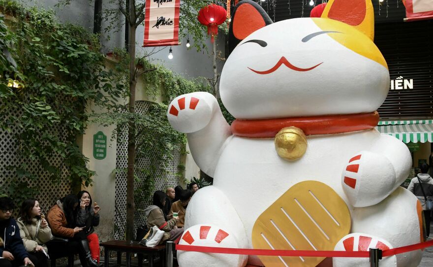 People eat ice cream next to a large cat statue at a shop in Hanoi this week. Cat statues of all sizes and styles line the streets of Vietnam ahead of the Lunar New Year.