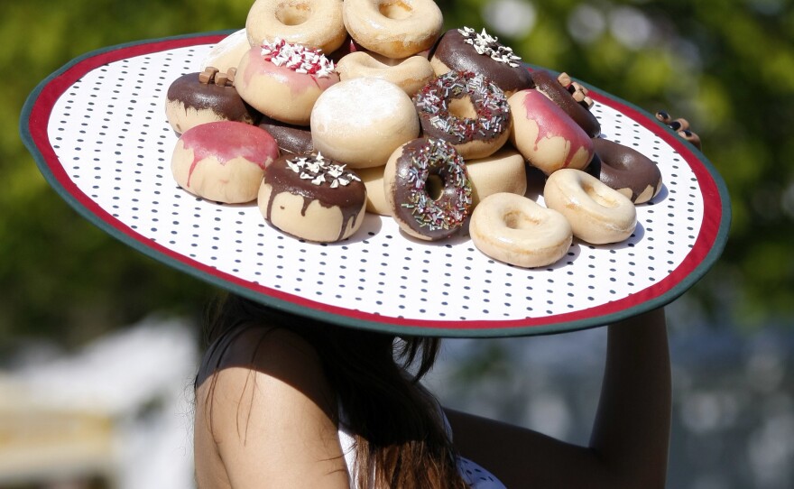 A woman, likely a doughnut/donut-lover, wears a hat resplendent in deep-fried goodies.