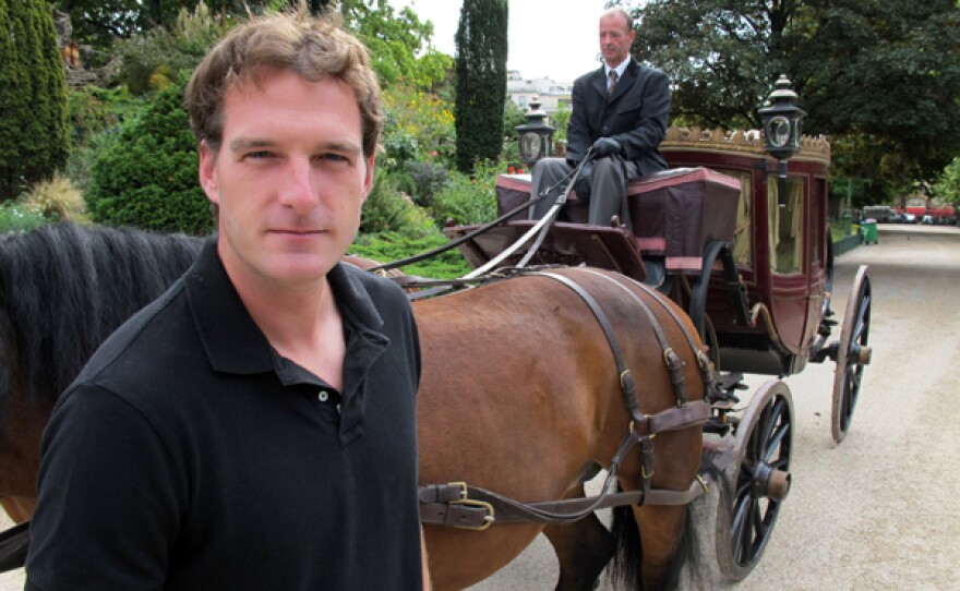 Host Dan Snow standing next to a horse and carriage.
