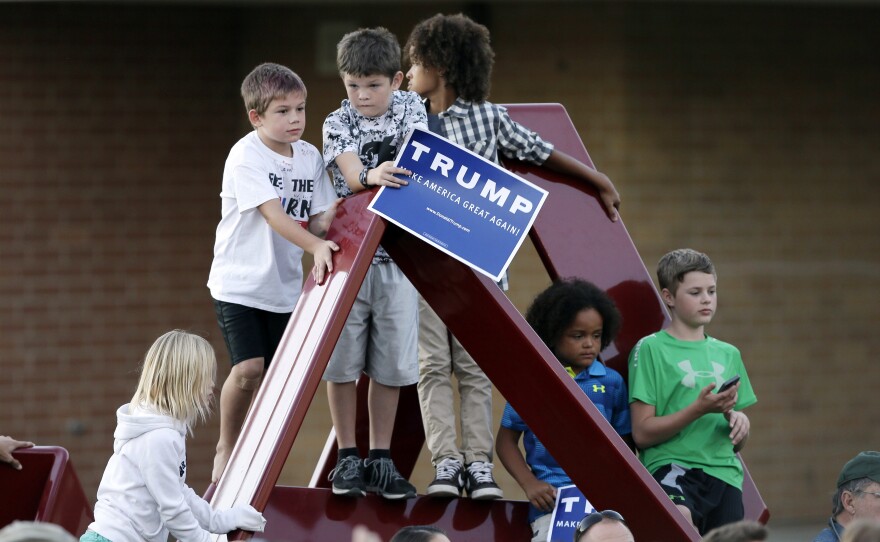 Children climb on a sculpture as Republican presidential candidate Donald Trump speaks during a rally at Urbandale High School, in Urbandale, Iowa.