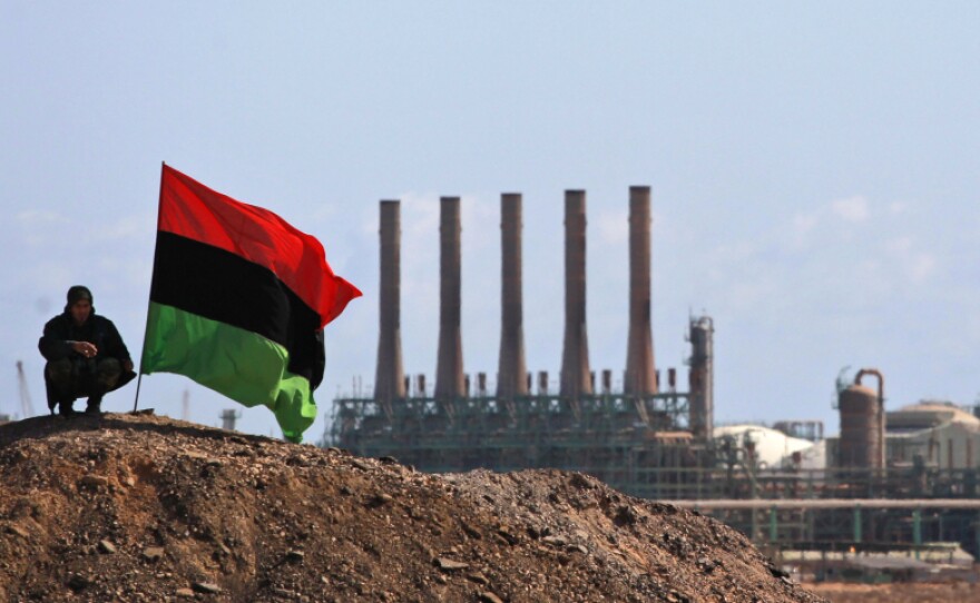 An opposition fighter perches next to a pre-Gadhafi flag as he stands guard outside the oil refinery in Ras Lanuf.