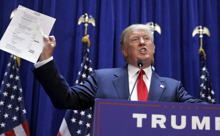 Donald Trump holds up a copy of what he says his net worth is in June 2015. It claims his net worth at almost $9 billion, though others have estimated it to be far lower.