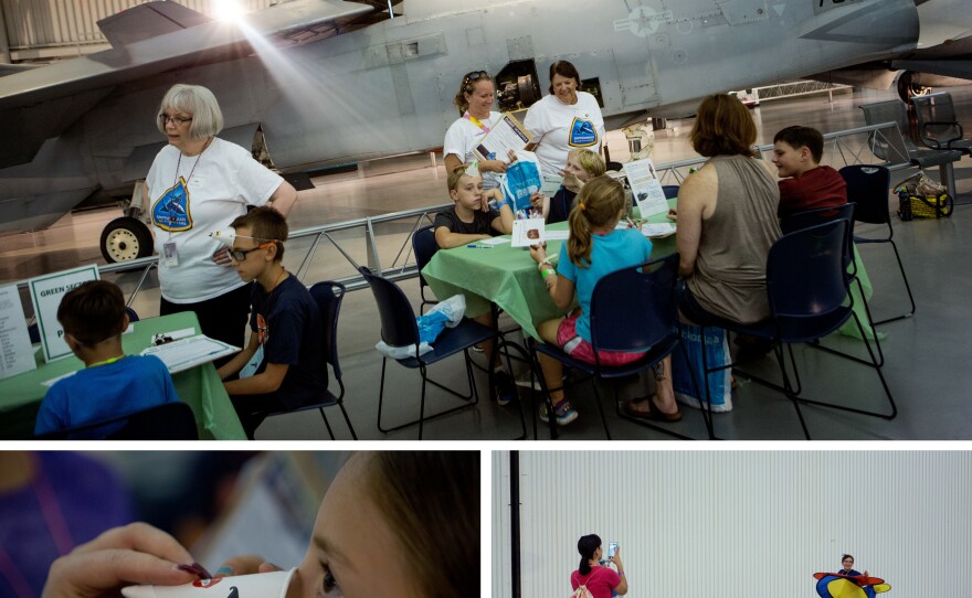 Sean Mclaughlin (top, center) sits with a friend as they pick out their pilot code names. Audrey Strauss, 8 (bottom, left), tries on her decorative "nose cone", inspired by the nose cone of a plane. Nathan Ferraro, 10 (bottom, right), plays the role of a plane during a marshaling activity as his mom, Cora, takes a photo.